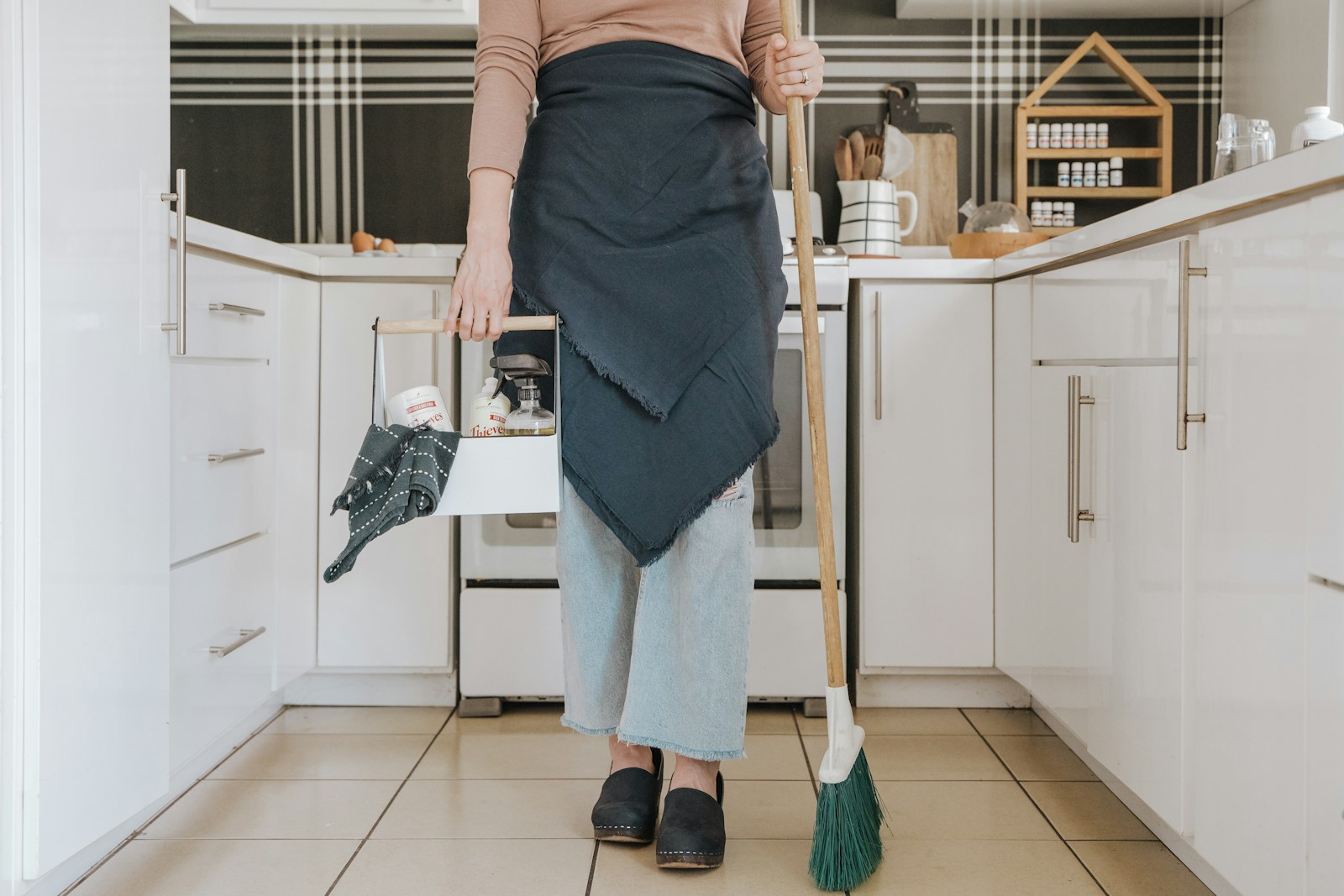 une femme debout dans une cuisine, tenant un balai d'un service de conciergerie immobilière