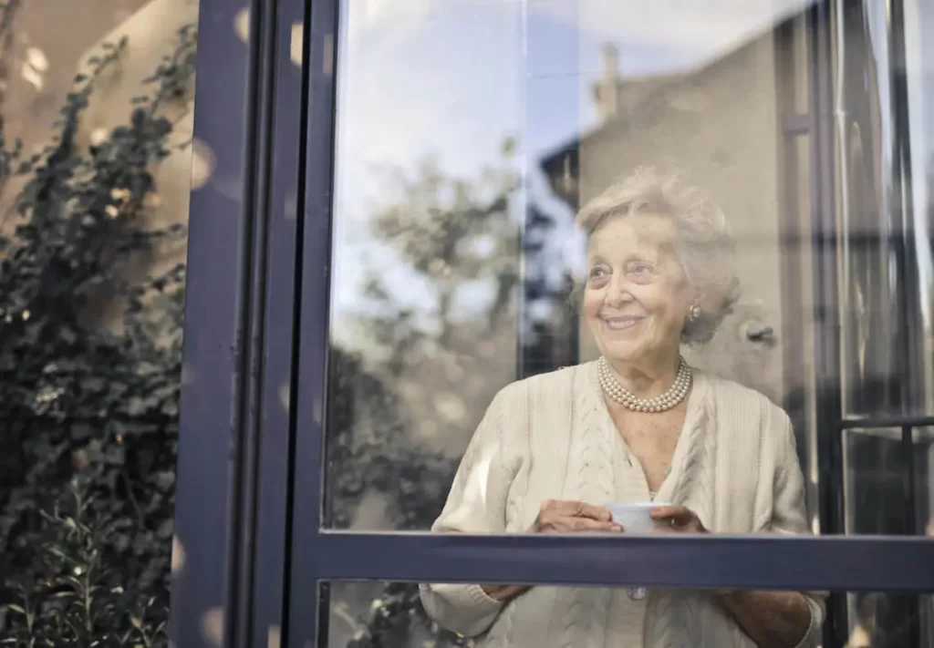 Femme âgée regardant au travers d'une fenêtre profitant des avantages d'un viager

